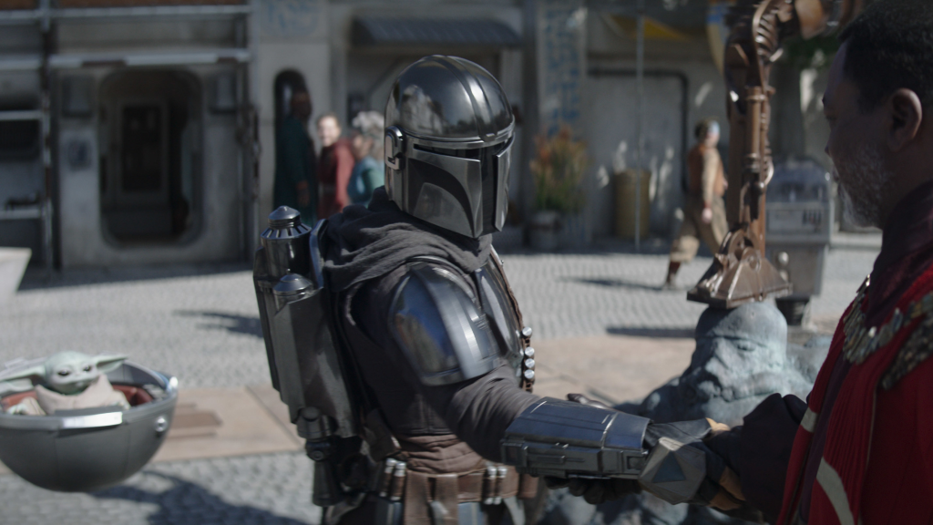 Pedro Pascal as Din Djarin in The Mandalorian with Grogu in the background